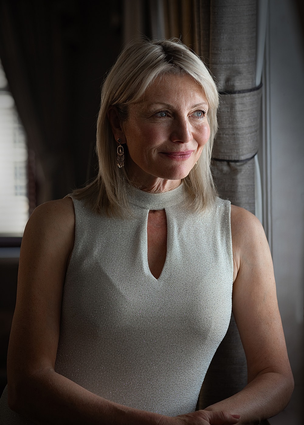 Woman in elegant dress, smiling by window.