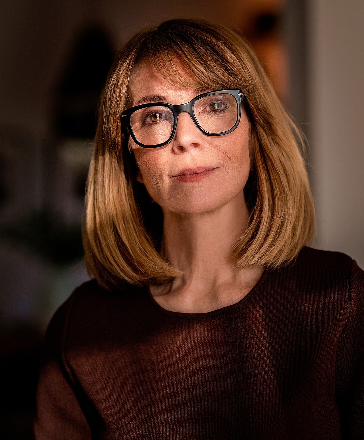 Woman with glasses in warm indoor light.