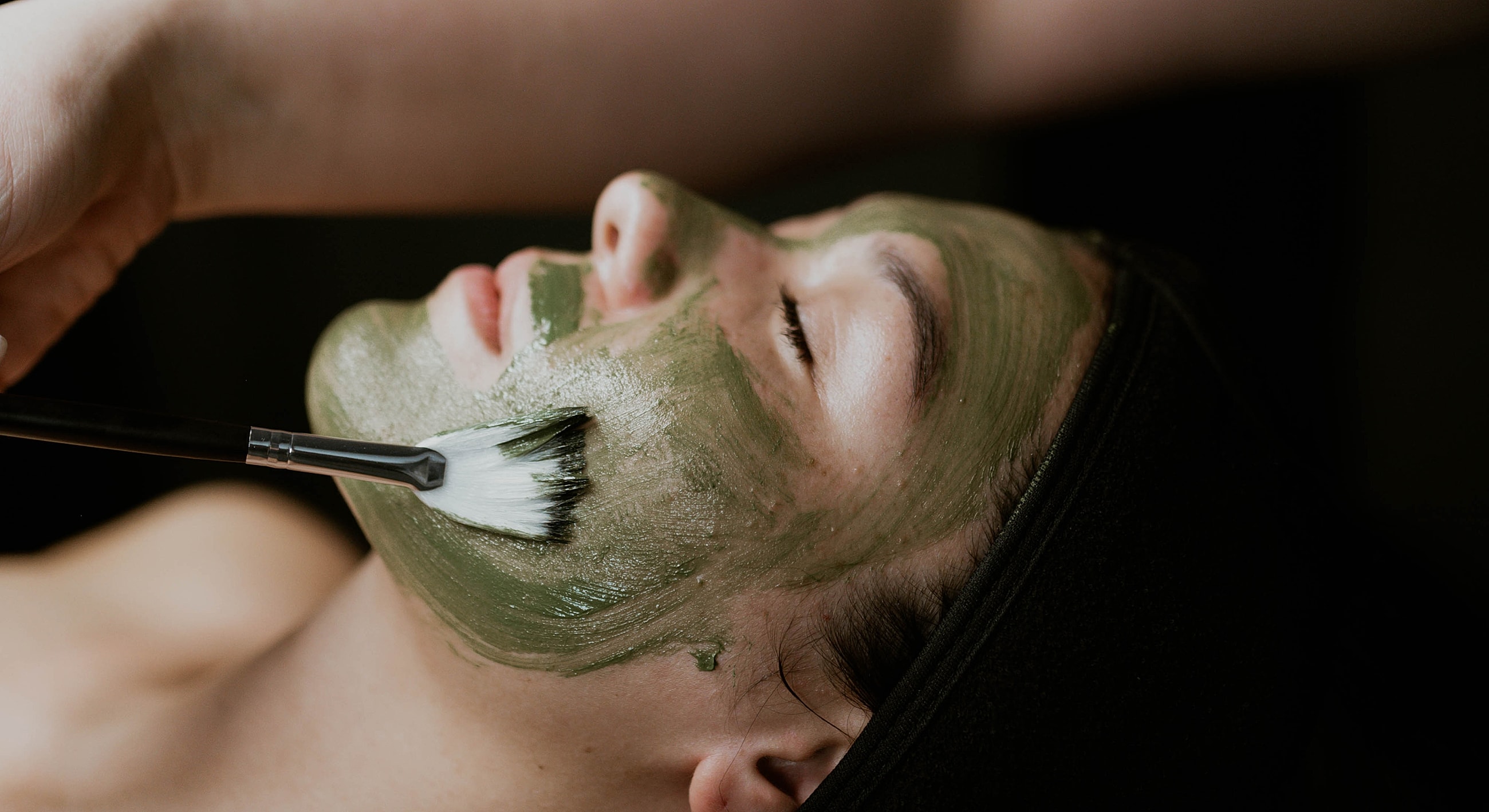Applying green facial mask during treatment session.