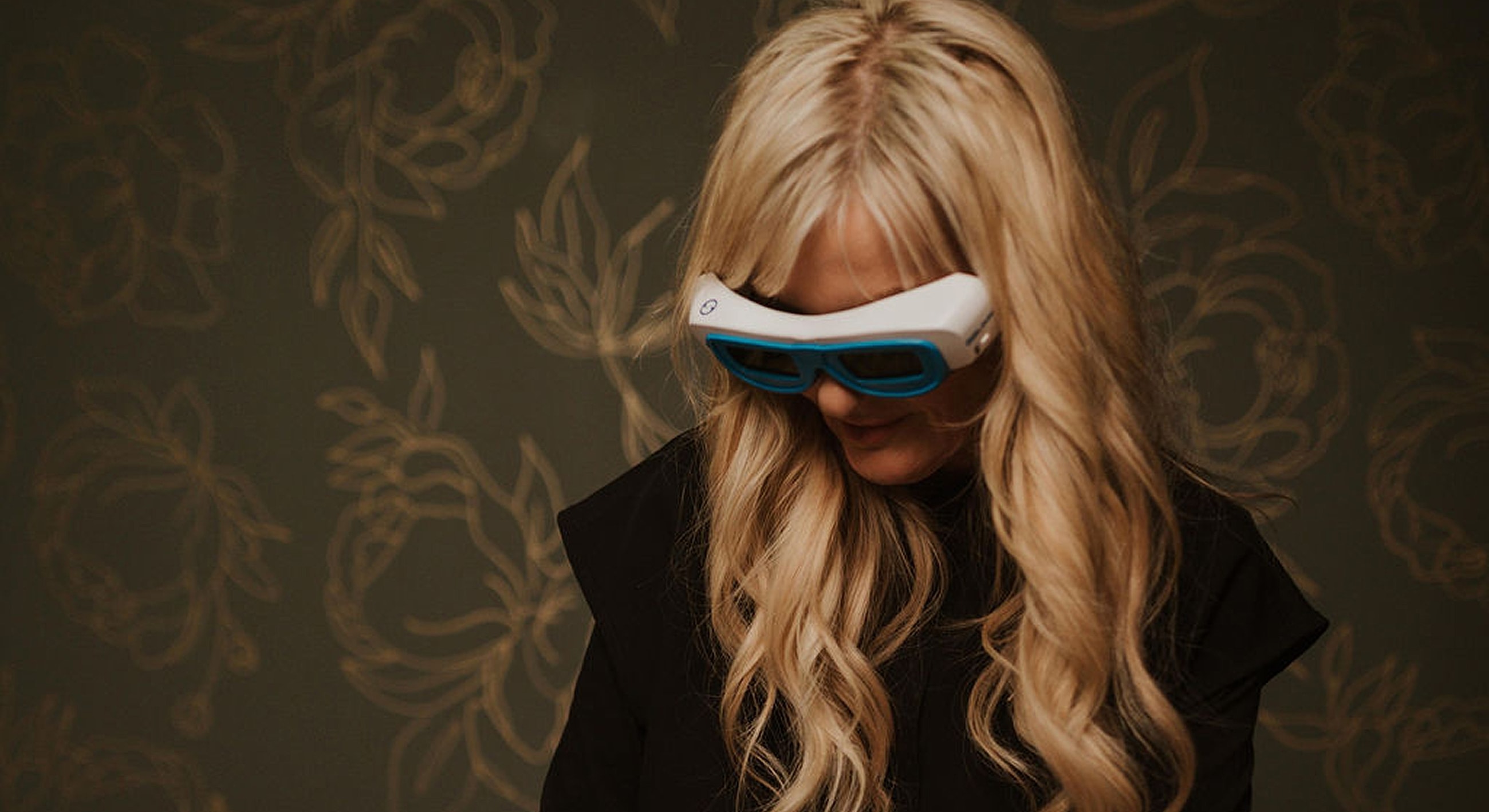 Person wearing futuristic eyewear against floral background.